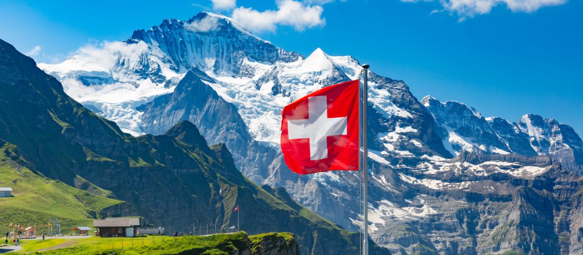 Swiss flag waving and tourists admire the peaks of Jungfrau mountain on a Mannlichen viewpoint, Bernese Oberland Switzerland